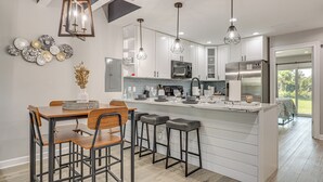 A modern kitchen with white cabinetry, a central island with stools, pendant lighting, and a view to the outdoors. - Ponte Vedra Beach Getaway w/ Patio! (Ponte Vedra Beach)