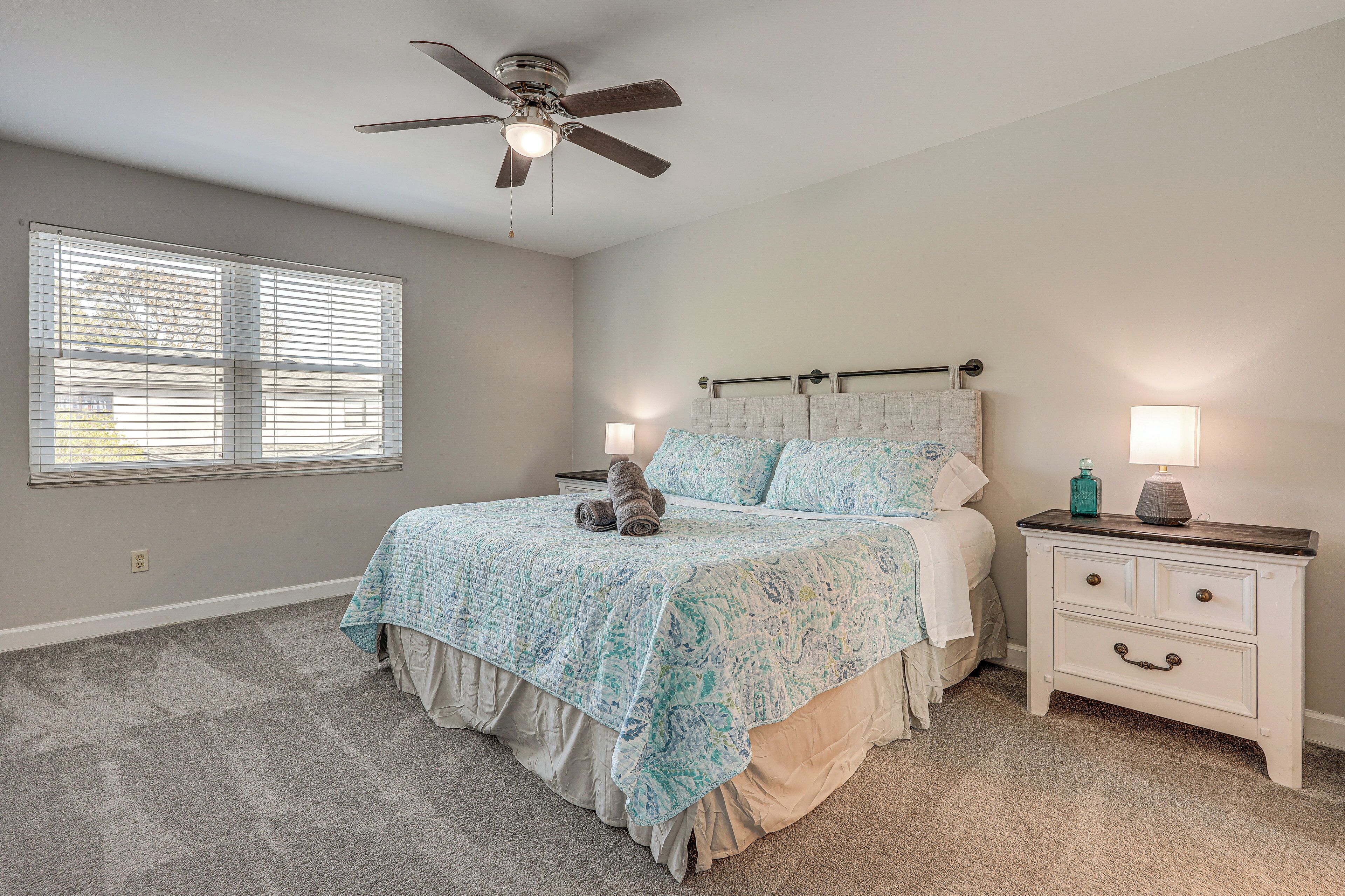 A bedroom with a bed, a nightstand, a ceiling fan, and a window with blinds.