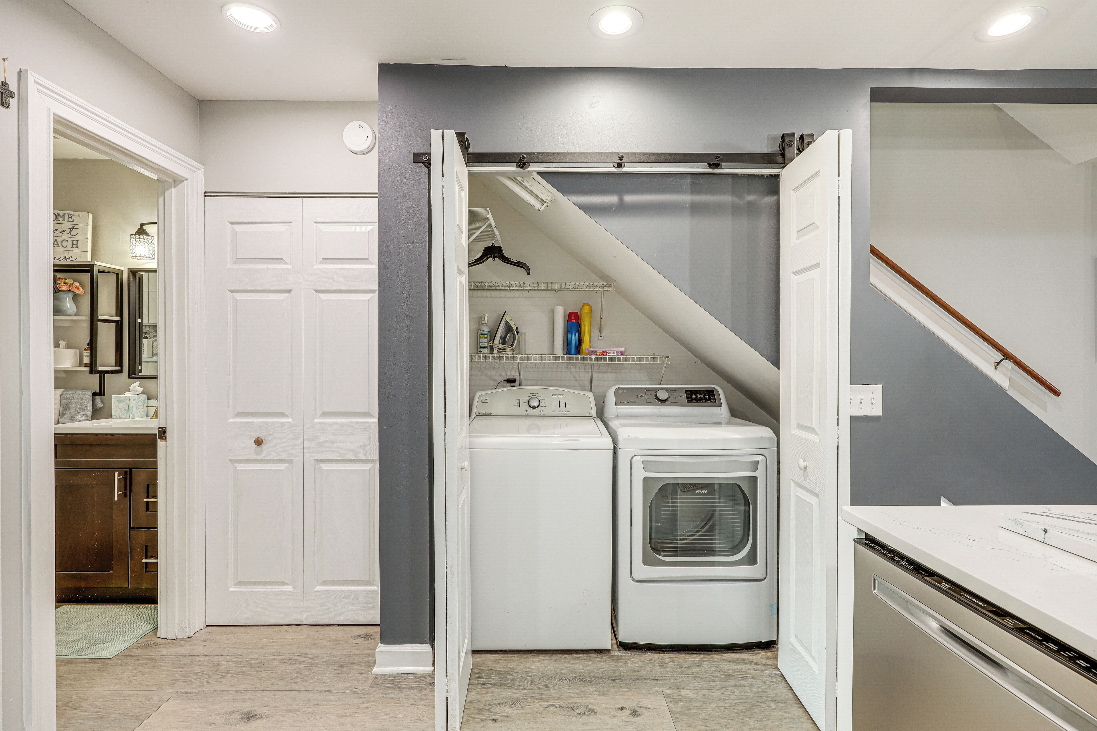 A laundry room with two washing machines and a dryer, a white door, and a staircase leading to another room.