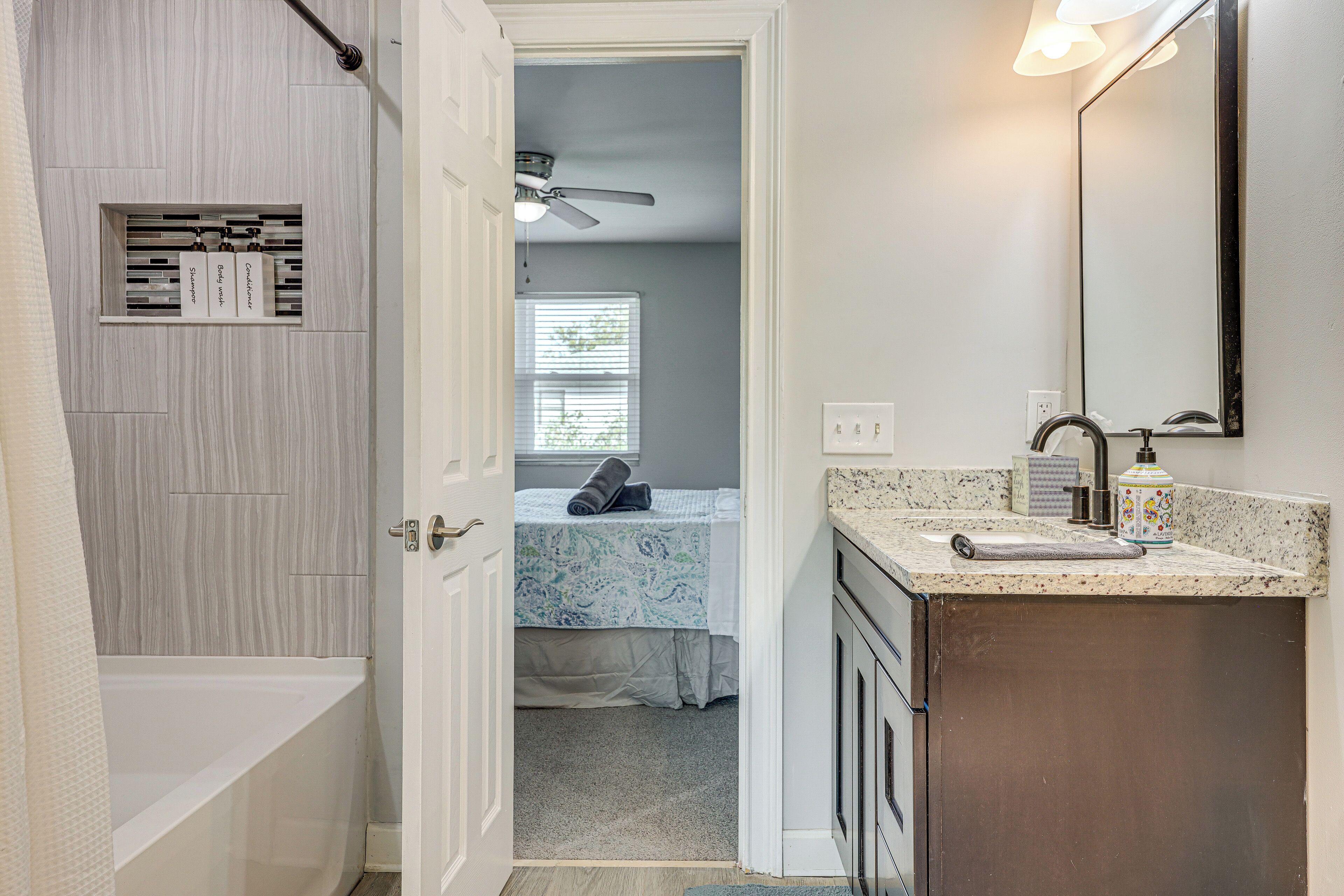 Une salle de bain avec une baignoire, un meuble-lavabo avec un miroir et un ventilateur de plafond.