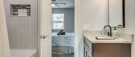 Une salle de bain avec une baignoire, un meuble-lavabo avec un miroir et un ventilateur de plafond.