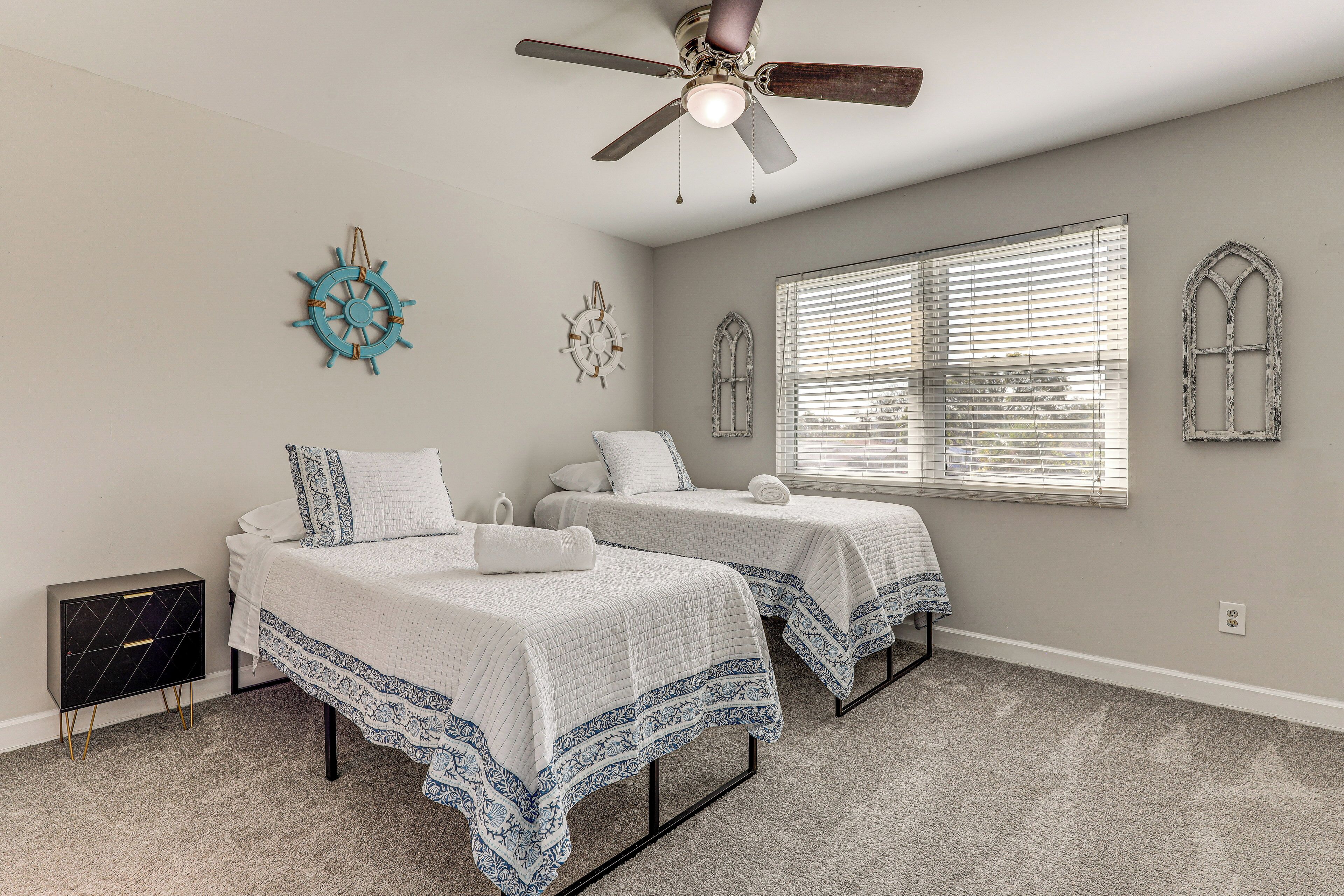 A bedroom with two beds, a ceiling fan, a window with blinds, and a decorative wall clock.