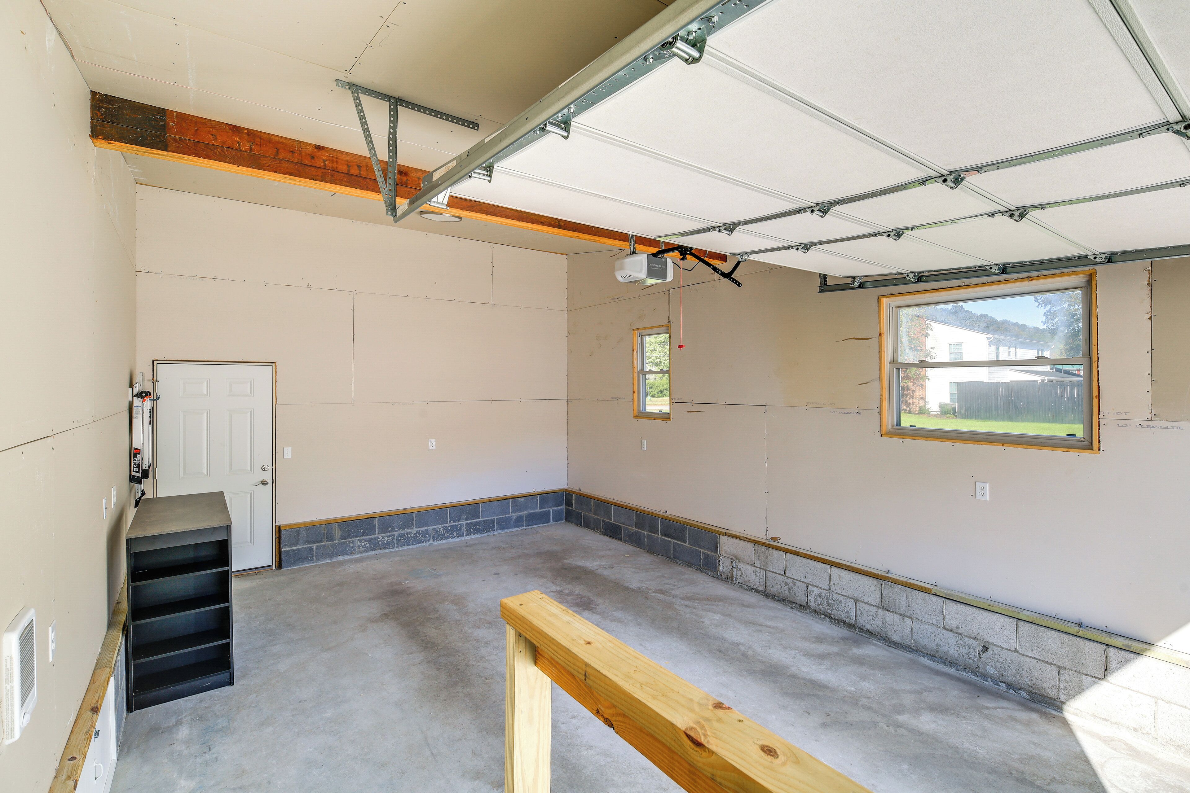 Een garage met een betonnen vloer, een houten deur en een raam dat uitkijkt op een tuin.
