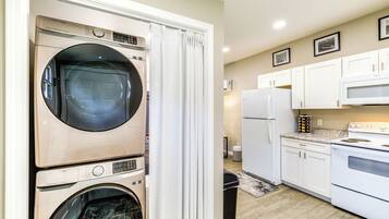 A compact kitchen with a built-in washer and dryer, white cabinets, a microwave, and a refrigerator.