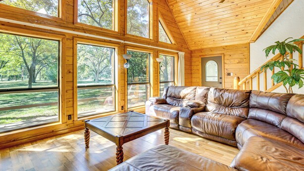 A spacious room with large windows, a leather sofa, a wooden coffee table, and a ceiling fan.
