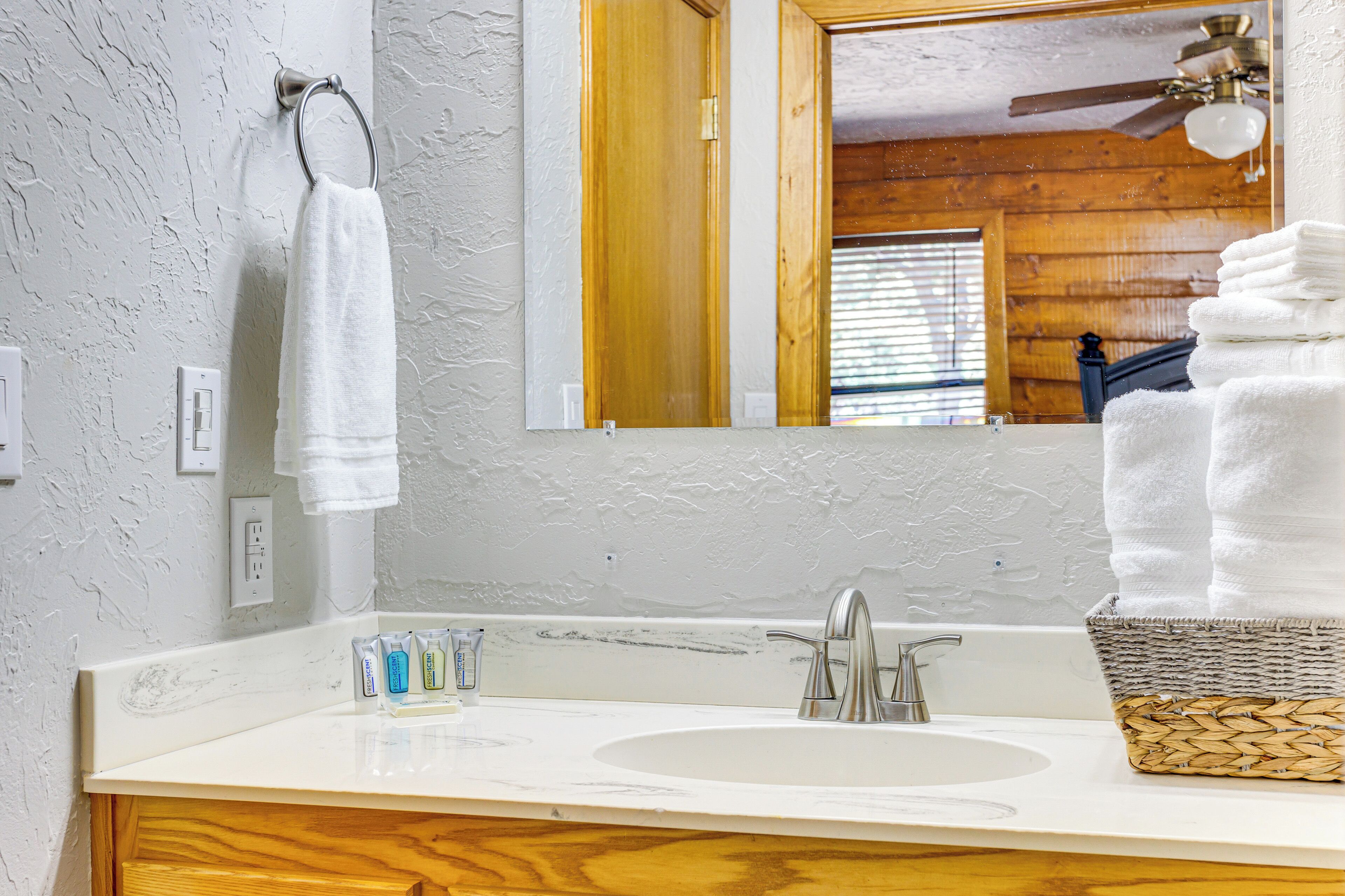 Une salle de bain avec un lavabo blanc, un meuble-lavabo en bois, un miroir et un ventilateur de plafond.