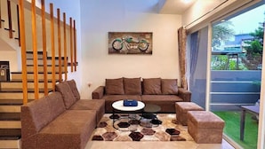 A modern living room with a brown sectional sofa, a coffee table, and a rug. A staircase with wooden railings is visible to the left. - Scarlet By Stellar Stays (Mawal)