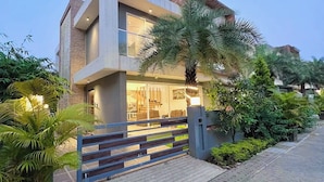 A modern two-story house with a large balcony, a gated entrance, and lush greenery. - Scarlet By Stellar Stays (Mawal)