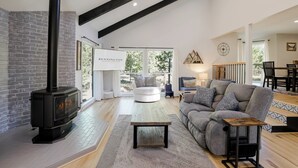 A spacious living room with a fireplace, a comfortable sofa, and a dining area. - NEWB07-Family-Friendly Sunriver Retreat | Hot Tub, A/C, Dog-Friendly, Sleeps 10 (Sunriver)