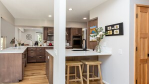 A modern kitchen with wooden cabinets, a central island, and bar stools. - NEWB07-Family-Friendly Sunriver Retreat | Hot Tub, A/C, Dog-Friendly, Sleeps 10 (Sunriver)