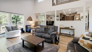 A spacious living room with a grey sofa, a wooden coffee table, and a white armchair. A dining area is visible in the background with a wooden table and chairs. - NEWB07-Family-Friendly Sunriver Retreat | Hot Tub, A/C, Dog-Friendly, Sleeps 10 (Sunriver)
