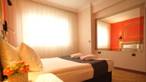 A hotel room with a large bed, a bedside table with a vase of flowers, a mirror on the wall, and a window with curtains. - Malabadi Otel (Diyarbakir)