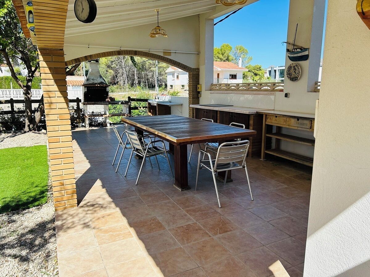 Une terrasse extérieure avec une table en bois et des chaises en métal, un mur en briques et une vue sur le quartier.