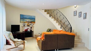 A living room with a sofa, a rocking chair, a TV, a fireplace, and a staircase. - SAONA VILLAS (VN LAURE): villa 8 people, private pool, wifi, beach 3.5 km (Les Tres Cales)