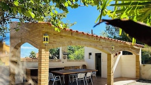 A covered outdoor patio with a brick archway, a wooden table with chairs, and a small decorative lantern. - SAONA VILLAS (VN LAURE): villa 8 people, private pool, wifi, beach 3.5 km (Les Tres Cales)