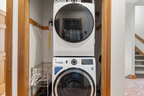 A laundry room with stacked washers and dryers, wooden paneling, and a tiled floor. - Ocean Crest: Oceanfront | Elevator | Pet-Friendly (Rodanthe)