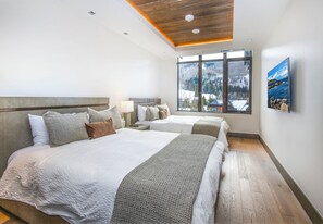 Une chambre d’hôtel moderne avec deux lits, de grandes fenêtres donnant sur les montagnes et un plafond en bois.