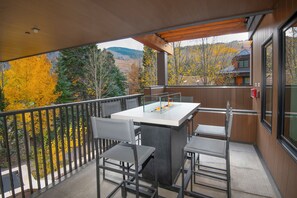 Un balcon avec une table et des chaises, donnant sur une forêt aux couleurs automnales.