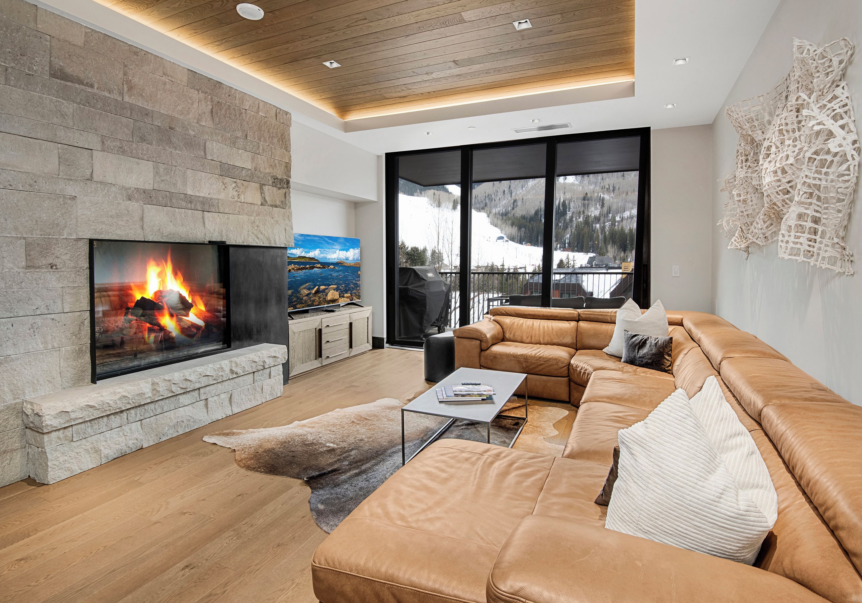 A modern living room with a stone fireplace, leather sofa, and large windows offering a mountain view.