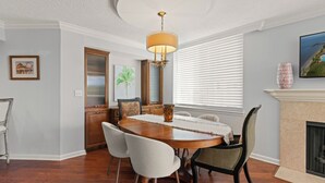 A dining room with a wooden table, white chairs, a vase, and a fireplace. - King and Prince Villa (St. Simons Island)