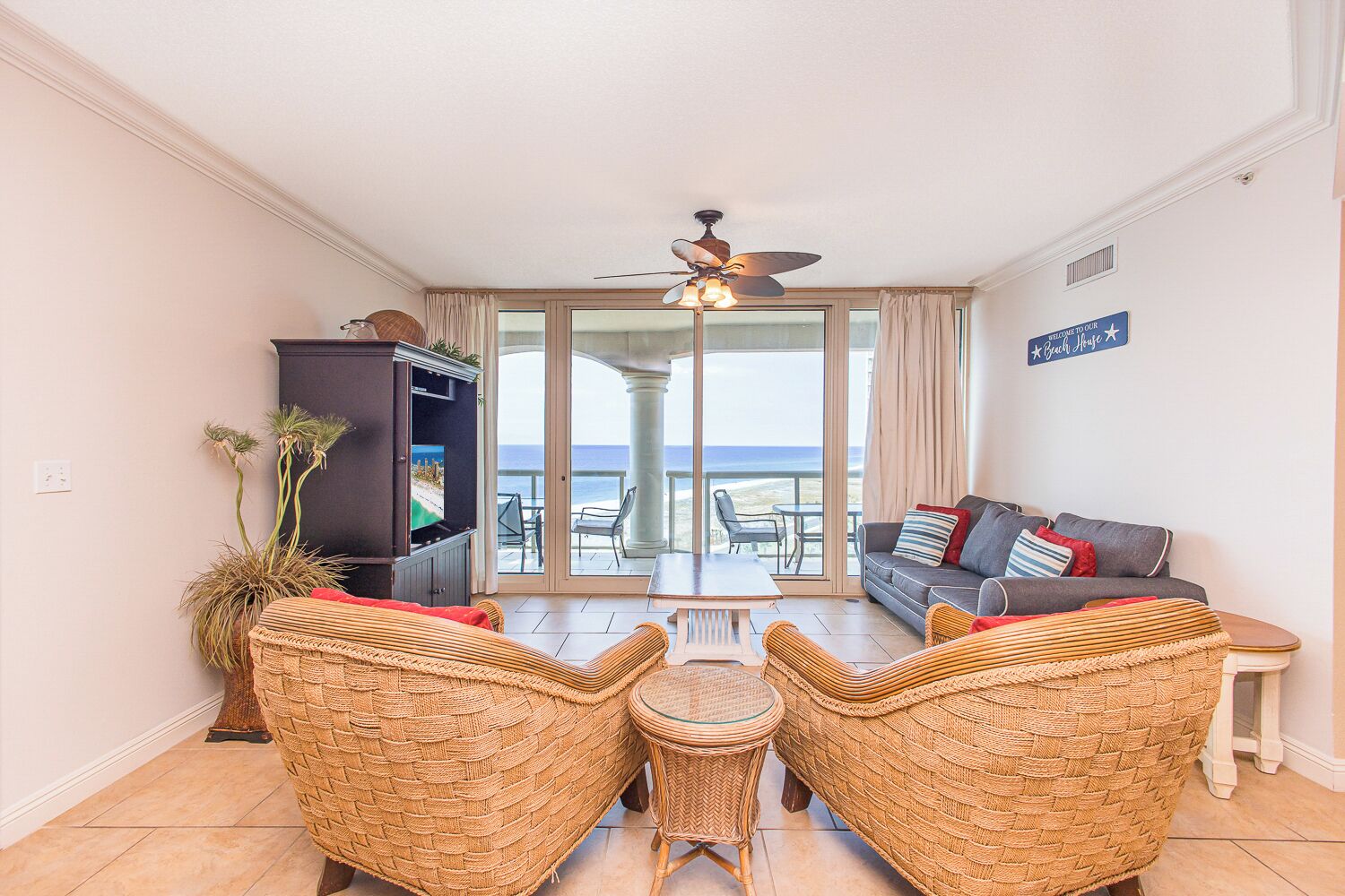 A living room with a television, wicker furniture, and a view of the beach.