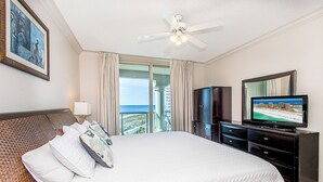 Ein Hotelzimmer mit einem großen Bett, einem Fernseher, einem Kleiderschrank und einem Balkon mit Blick auf den Strand.