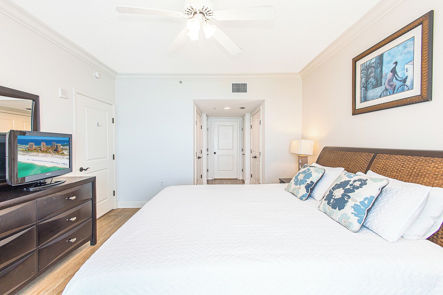 A hotel room with a large bed, a television on a dresser, a door leading to another room, and a painting on the wall.