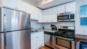 A kitchen with white cabinets, a stainless steel refrigerator, a microwave, a dishwasher, and a stove. - Boston Apartment | near T (Boston)