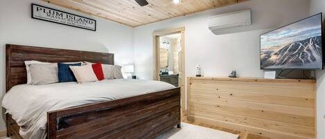 A bedroom with a wooden ceiling, a bed with a headboard, a dresser, a television, and a sign that reads "PLUM ISLAND MASSACHUSETTS."