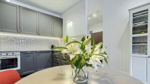 A modern kitchen with grey cabinets, a white countertop, and a vase with white flowers on a round table.