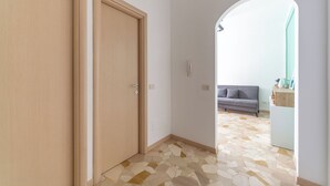 A hallway with a tiled floor, a wooden door, and a grey sofa in the background. - Milan Style Apartment  (Milan)