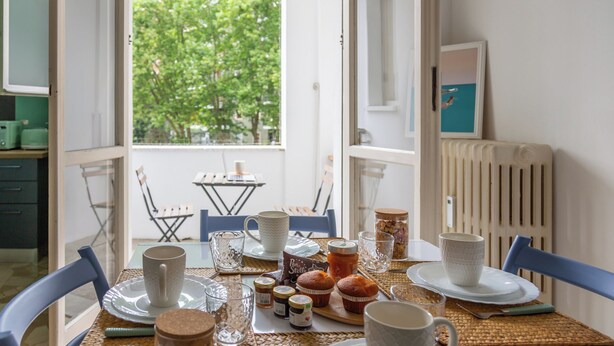 A dining table set with plates, cups, and food items, with a view of greenery outside. - Milan Style Apartment  (Milan)