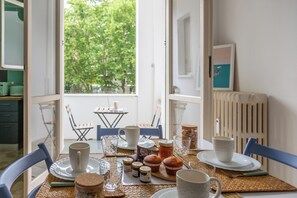 Una mesa de comedor dispuesta con platos, vasos y comida, con vistas a la vegetación exterior.