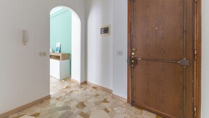 A hallway with a wooden door, a tiled floor, and a view into another room with a light blue wall and a counter. - Milan Style Apartment  (Milan)