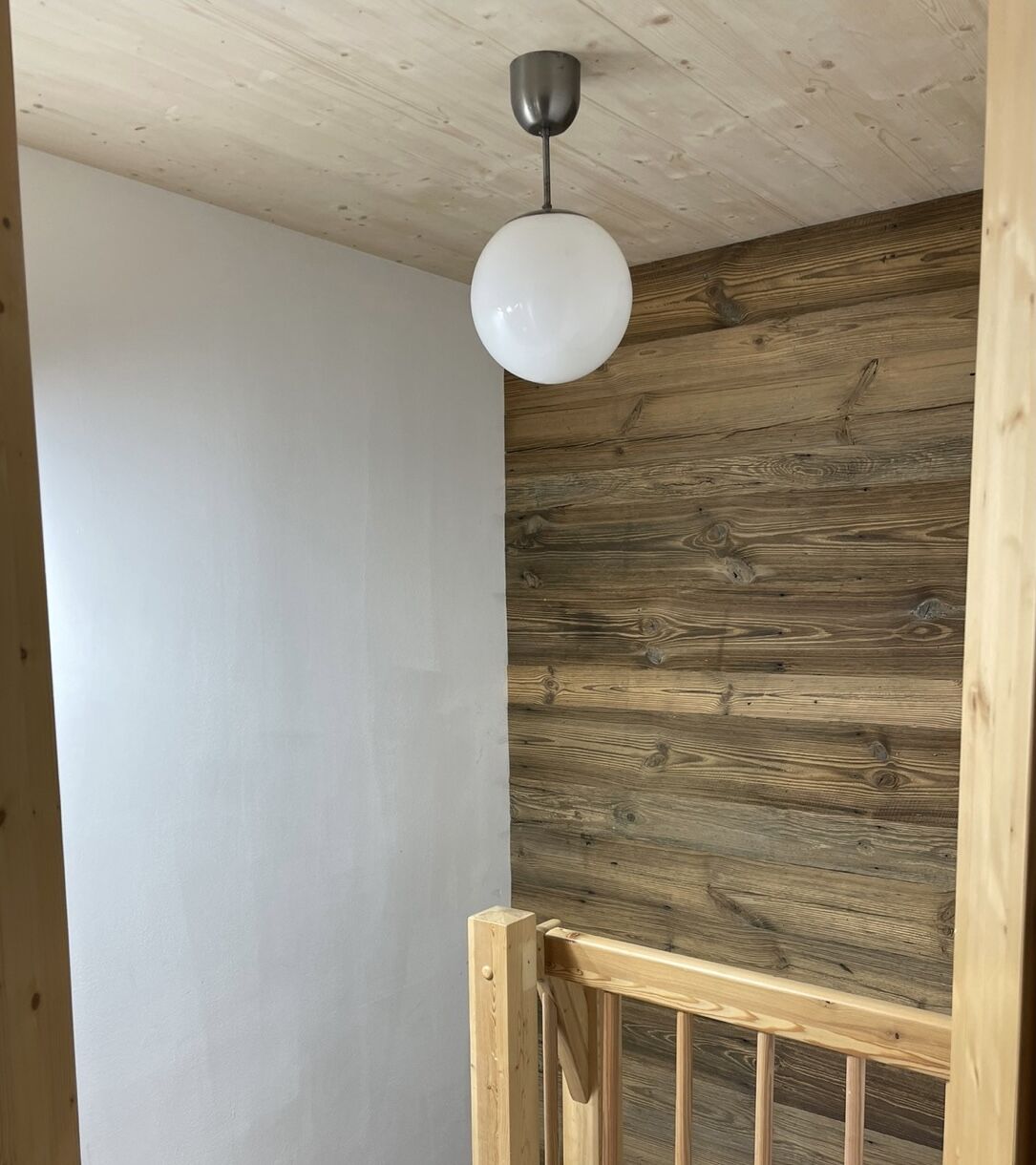 A wooden ceiling with a white wall and a wooden railing.