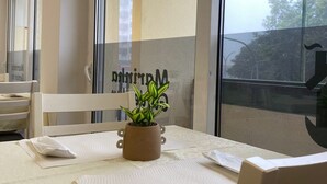Ein Essbereich mit Tisch für zwei Personen, einem Topfpflanzen und Blick durch ein großes Fenster.