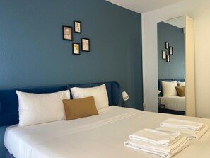 A hotel room with a large bed, white linens, a blue headboard, a brown pillow, and a mirror reflecting the room. - Marinha Garden Inn (Marinha Grande)