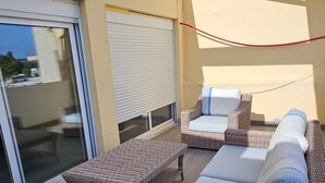 Ein Balkon mit Korbmöbeln, darunter eine Sitzecke, zwei Sessel und ein kleiner Tisch.
