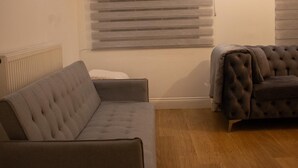 Una sala de estar con un sofá gris, otro sofá de gris más oscuro y suelo de madera.