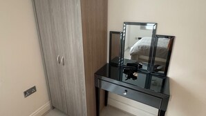 Una habitación con armario, tocador con espejo y una pequeña mesa.