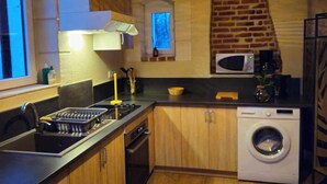A compact kitchen with wooden cabinets, a built-in oven, a microwave, and a washing machine. - Former gatehouse, spa, billiards room near Beauval Zoo, Loire château. (Luçay-le-Mâle)