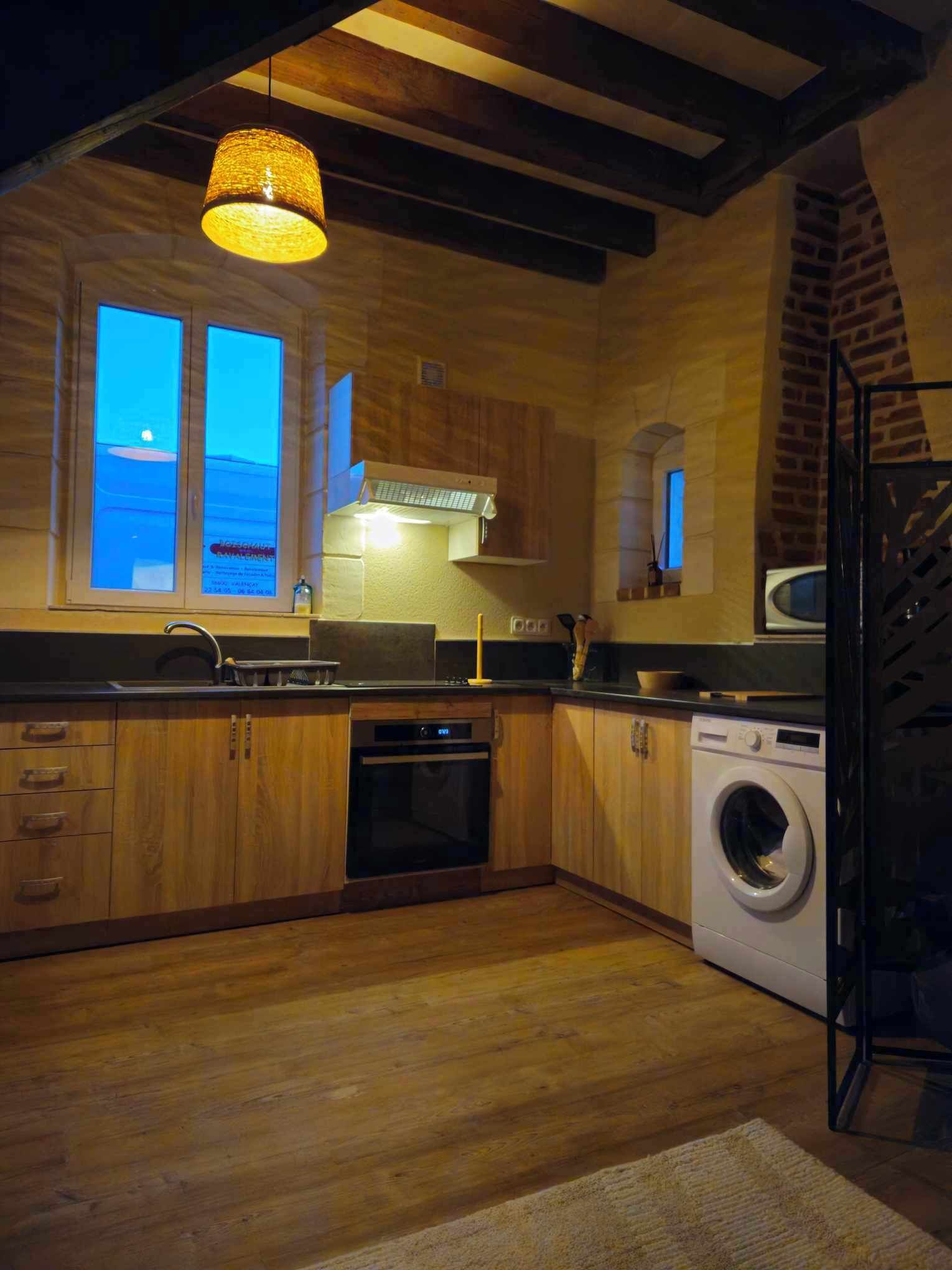 Une cuisine moderne avec des meubles en bois, un four encastré, un lave-linge et une grande fenêtre offrant une belle vue.