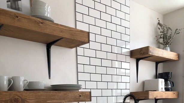Una cocina moderna con estantes de madera, armarios blancos y salpicadero de azulejos.