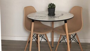 Una mesa redonda con cubierta de mármol, dos sillas de mimbre, una planta en maceta y un colgador de luz.