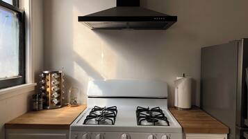 Una cocina con estufa blanca, extractor de humos negro y una ventana.