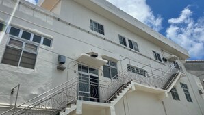 A multi-story building with a white facade, multiple windows, and a central staircase with metal railings. - One Miyakojima (Miyakojima)