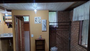 A compact living space with a bathroom, a small shelf, a hanging rack, and a brick wall. - ALDEA zen chalés e suítes privativos (Ouro Preto)