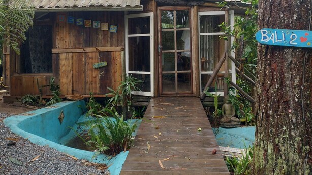 A rustic wooden cabin with a tiled roof, a wooden deck, and a small pond. - ALDEA zen chalés e suítes privativos (Ouro Preto)