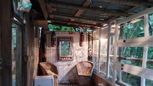 A rustic wooden room with a wooden bench, two wicker chairs, a small table, and a window with a view of greenery. - ALDEA zen chalés e suítes privativos (Ouro Preto)