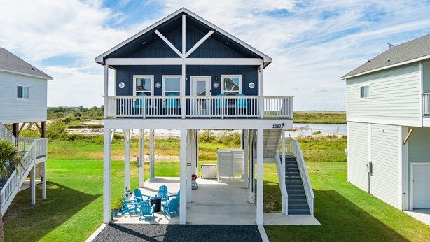 Een huis met twee verdiepingen, een balkon, een overdekte patio met tuinmeubilair en uitzicht op het strand.